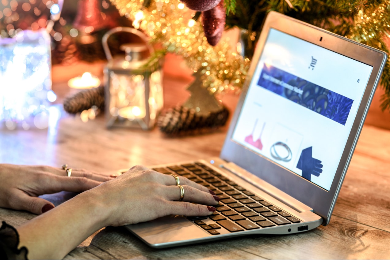 woman holiday shopping on a computer with a Christmas tree in the background