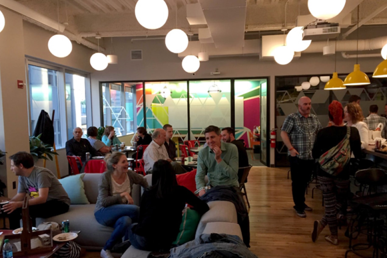 People in a cafe chatting with each other on couches, at tables, and at a cafe bar. 