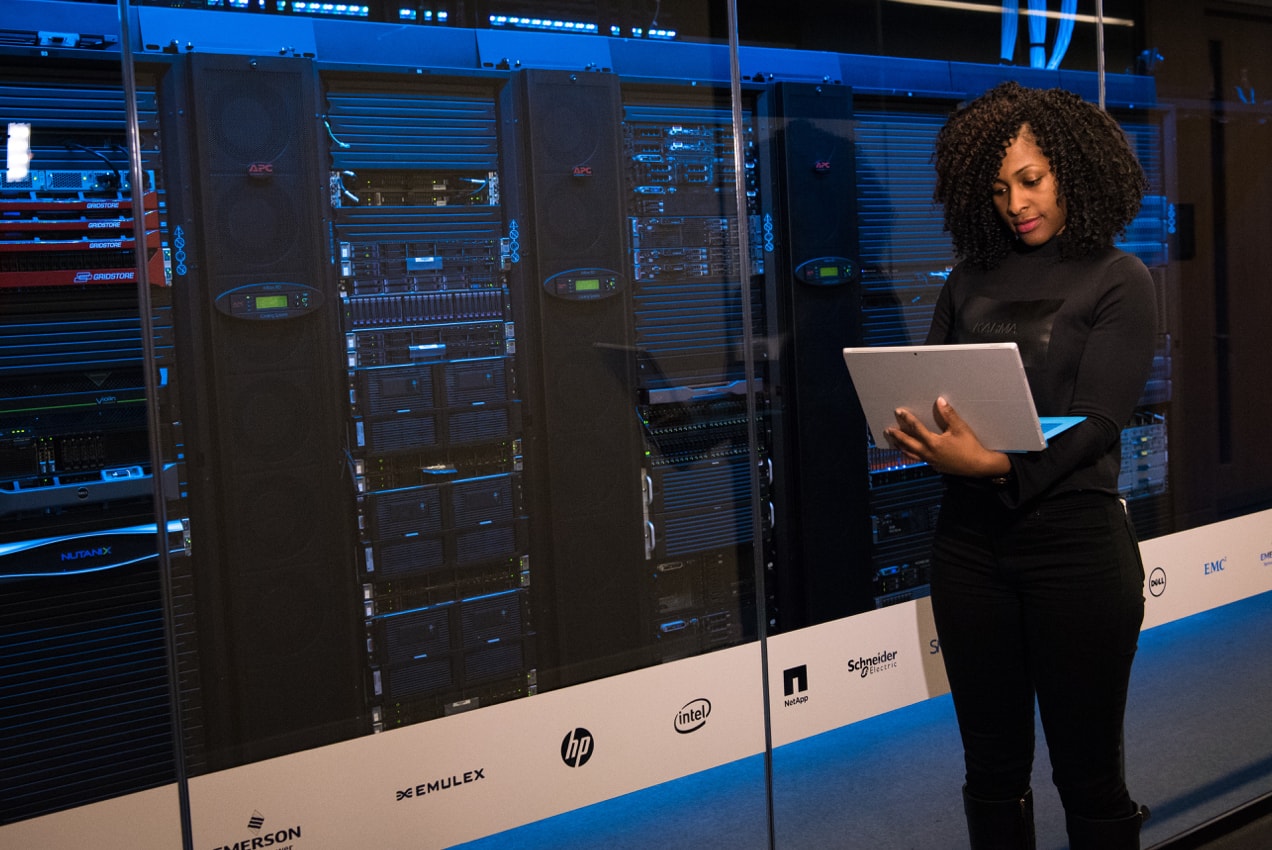 woman looks at a computer while standing in front of servers