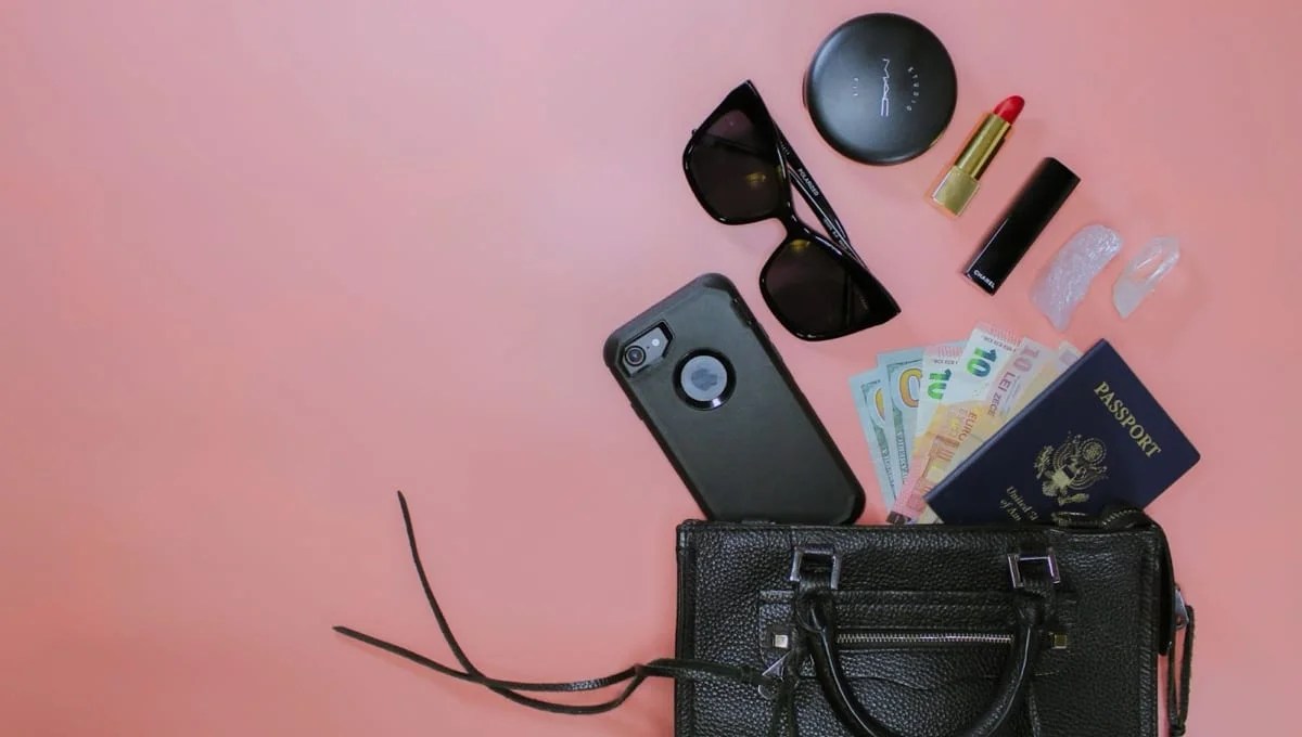 black bag with travel items on a pink background