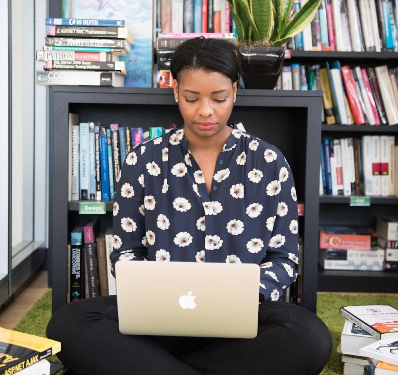 woman working on her laptop in front of a bookshelf