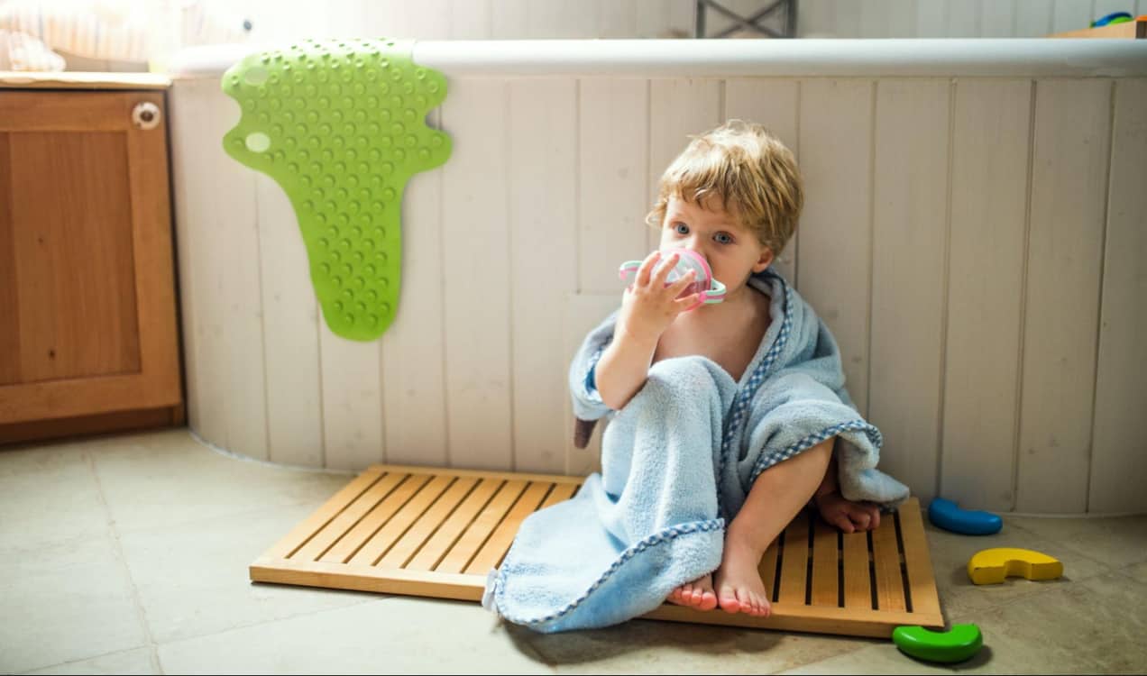 toddler in front of a bath tub wrapped in a blue towel