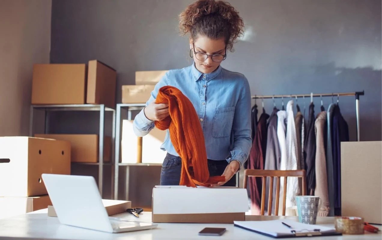 woman packing a piece of clothing in a box to ship