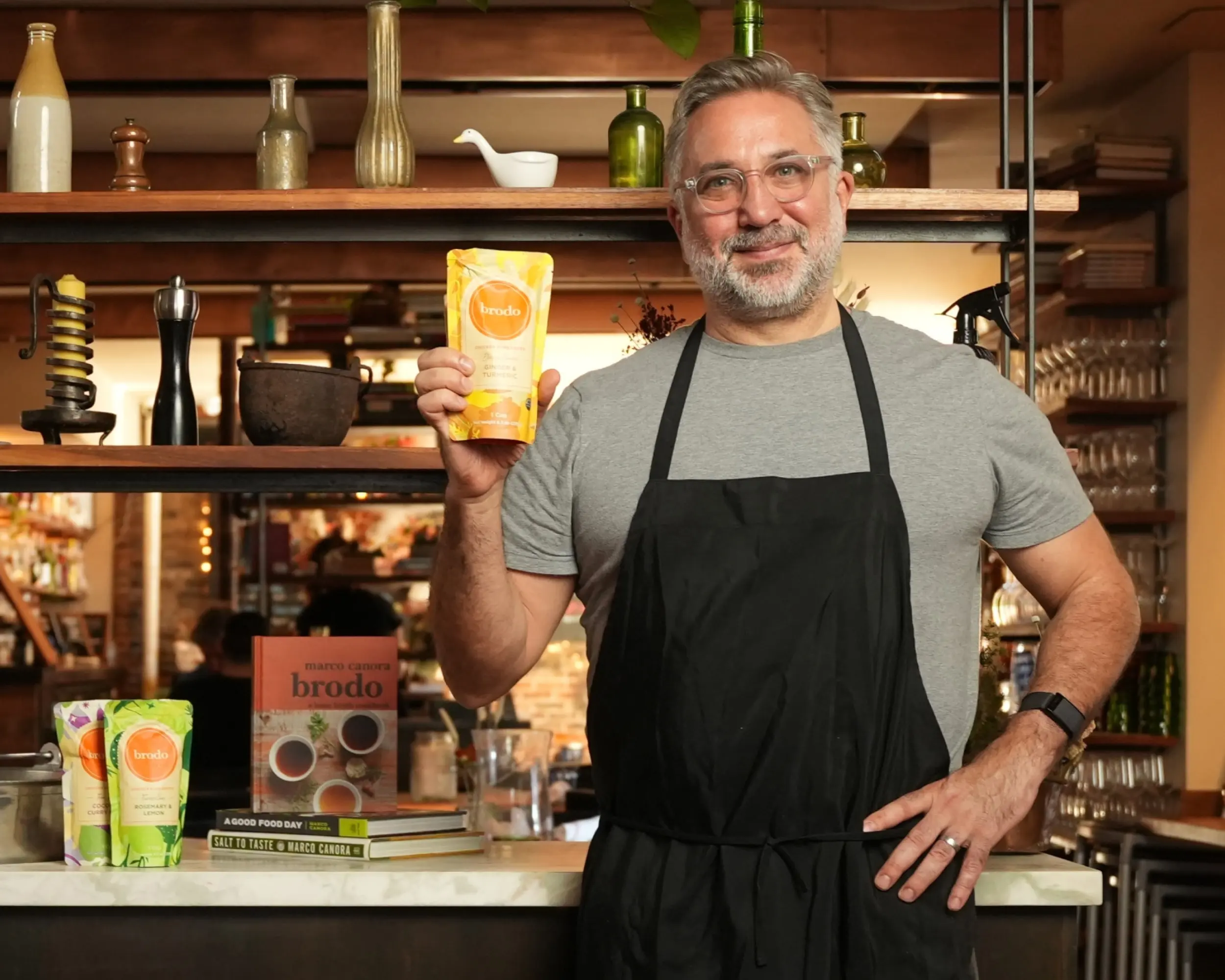 The owner of Brodo Broth Company poses in the restaurant kitchen with a Brodo Broth product.