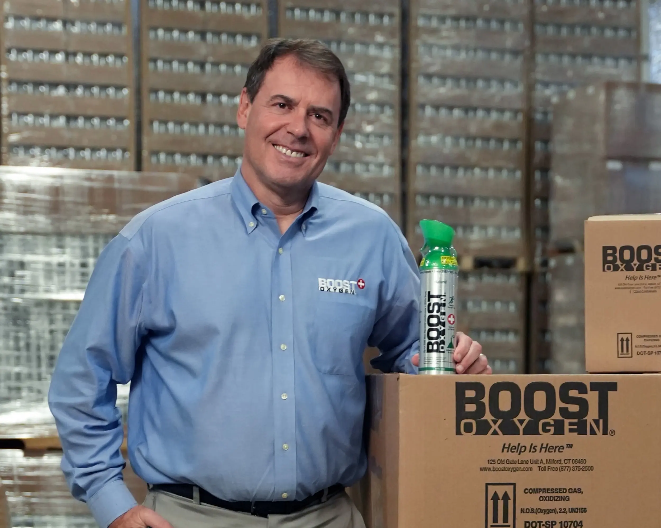 The owner of Boost Oxygen poses in a warehouse with a Boost Oxygen product.