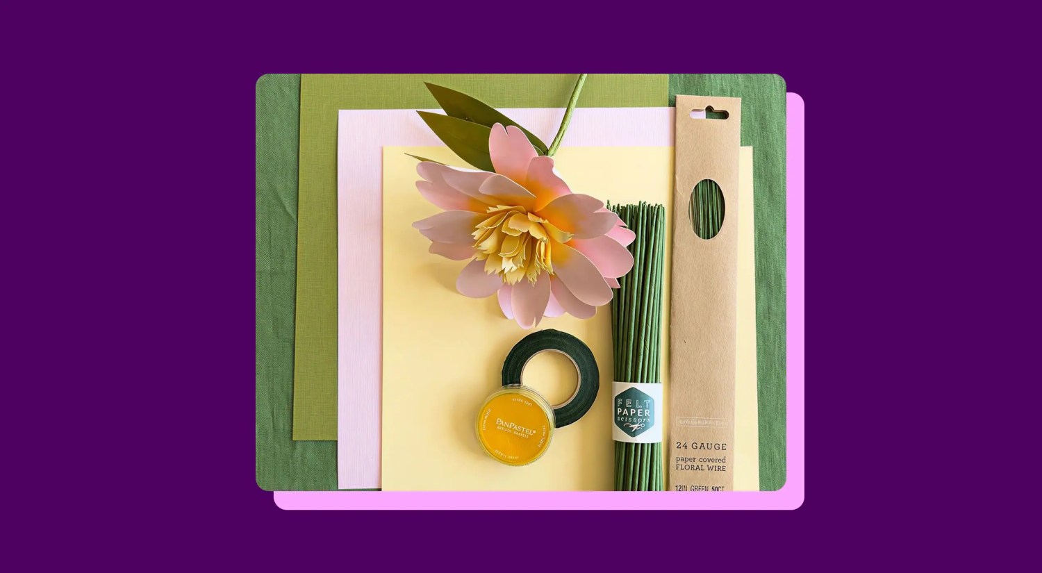a photo of a paper flower, sheets of paper, and other craft materials on a dark pink background
