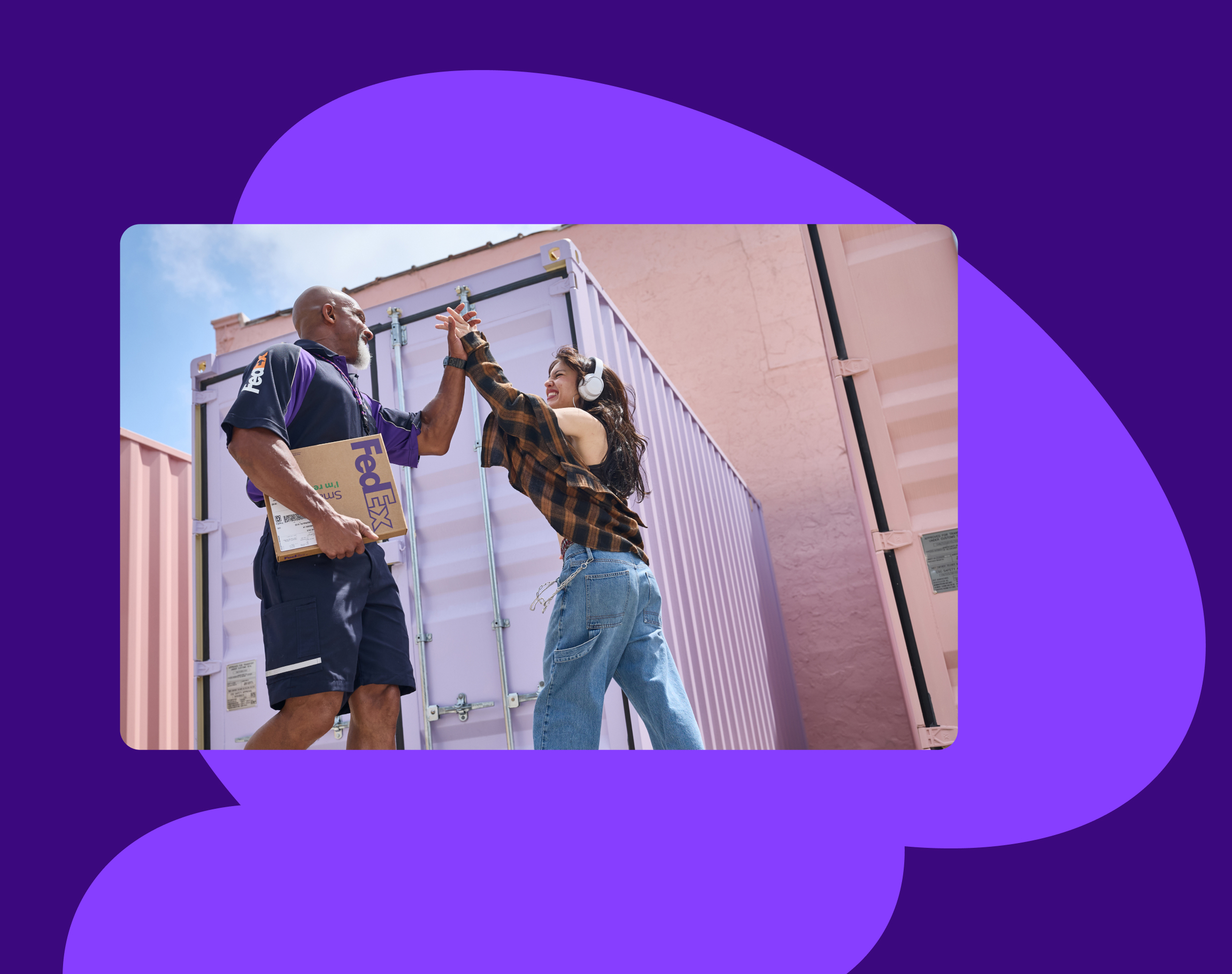 A FedEx driver and a cool-looking customer high five in front of a shipping container